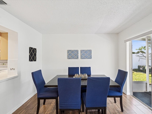 dining area featuring a textured ceiling, wood finished floors, visible vents, and baseboards