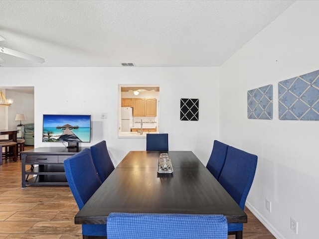 dining room featuring visible vents, a textured ceiling, ceiling fan, and wood finished floors