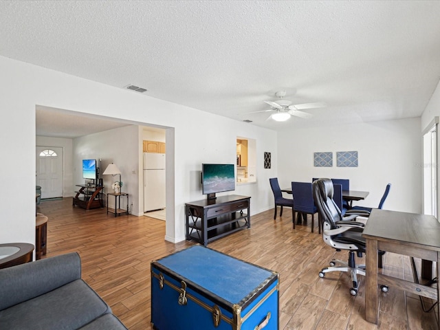 office space featuring visible vents, a ceiling fan, a textured ceiling, wood finished floors, and baseboards