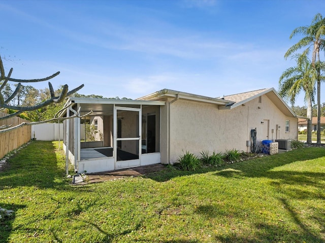 rear view of house with fence, a yard, a sunroom, central AC, and stucco siding