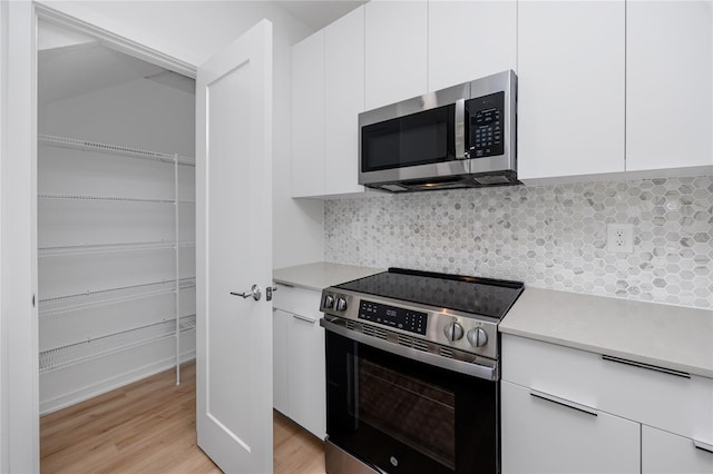 3402 E 28th Ave Unit 7, Tampa, FL 33605 - kitchen with stainless steel appliances, light countertops, white cabinets, light wood-style floors, and decorative backsplash