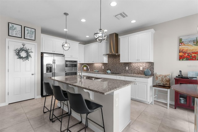 kitchen with stainless steel appliances, wall chimney exhaust hood, a sink, tasteful backsplash, and dark stone countertops