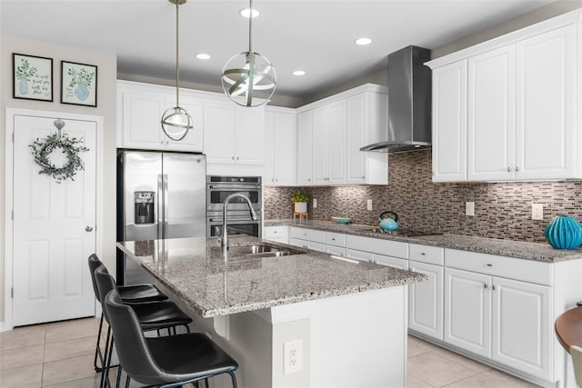 kitchen with wall chimney range hood, appliances with stainless steel finishes, a sink, light tile patterned floors, and recessed lighting