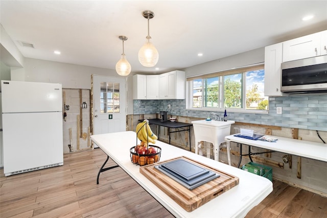 kitchen featuring stainless steel microwave, white cabinetry, light wood-style floors, and freestanding refrigerator