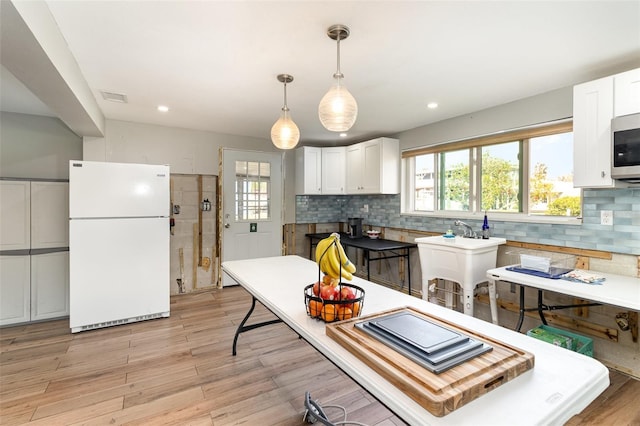 kitchen with tasteful backsplash, visible vents, light wood-type flooring, freestanding refrigerator, and white cabinetry