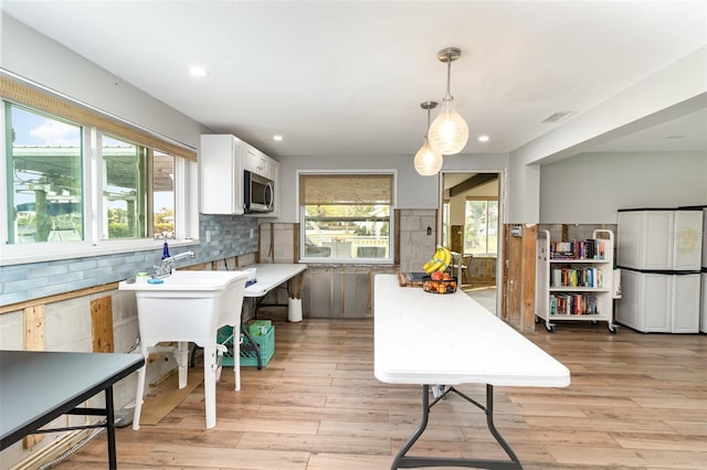 kitchen featuring light wood-type flooring, stainless steel microwave, backsplash, and freestanding refrigerator