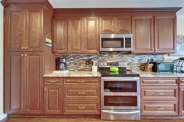 kitchen featuring light stone counters, decorative backsplash, brown cabinets, and stainless steel appliances