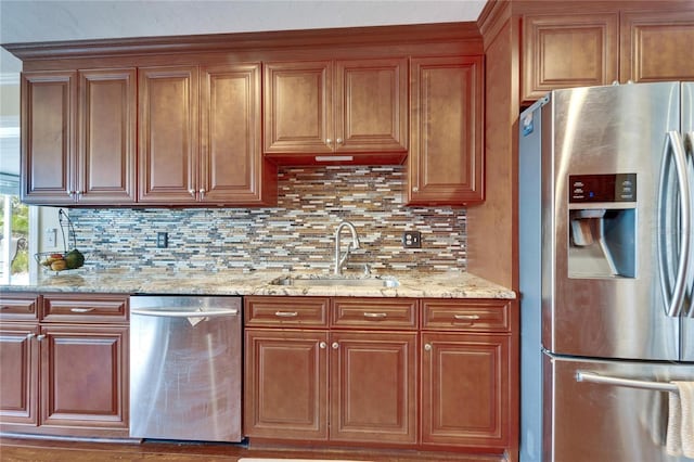 kitchen featuring a sink, light stone counters, stainless steel appliances, brown cabinetry, and decorative backsplash