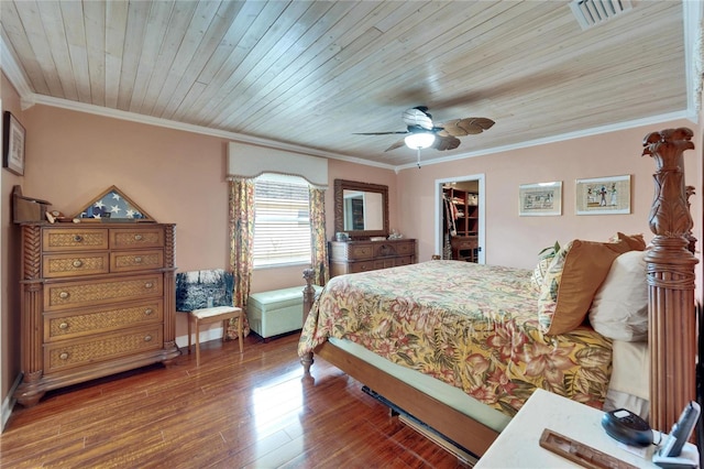 bedroom with a walk in closet, wood finished floors, visible vents, and ornamental molding