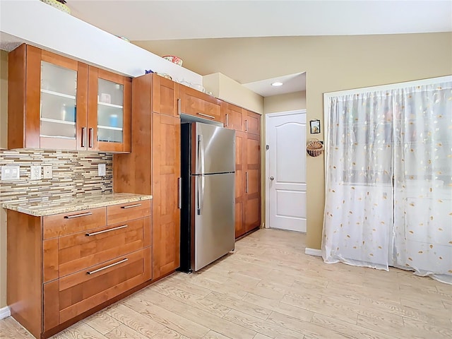 kitchen with lofted ceiling, brown cabinets, light wood-style flooring, and freestanding refrigerator