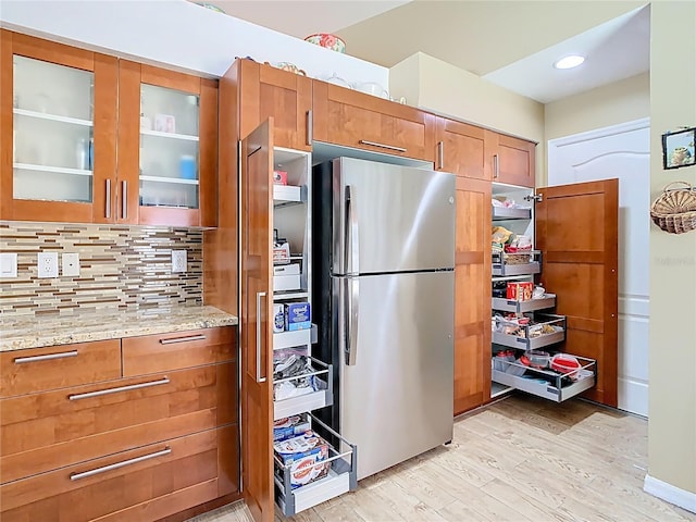 kitchen with light stone counters, light wood finished floors, brown cabinetry, and freestanding refrigerator