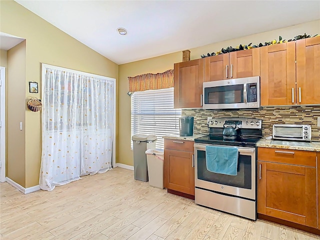 kitchen featuring brown cabinets, a toaster, vaulted ceiling, appliances with stainless steel finishes, and tasteful backsplash