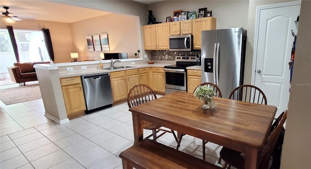 kitchen featuring stainless steel appliances, open floor plan, a sink, and light brown cabinetry