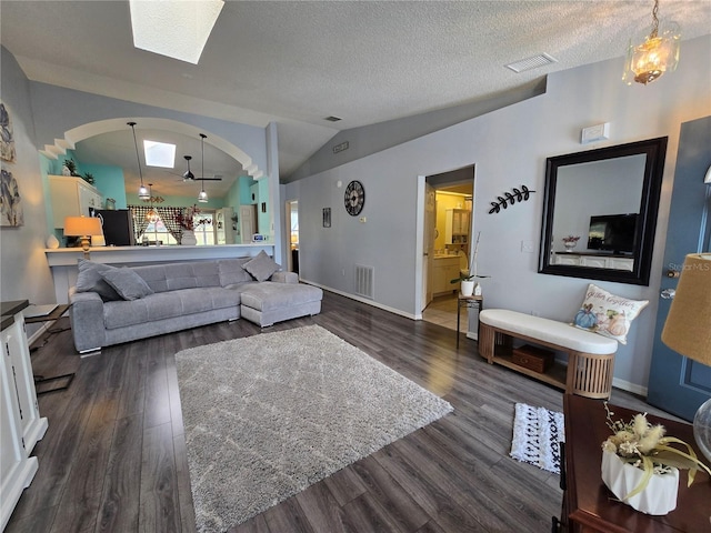 living room featuring dark wood-style floors, visible vents, vaulted ceiling with skylight, and a textured ceiling