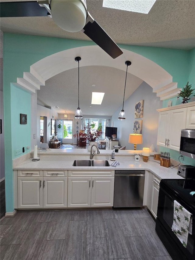 kitchen with pendant lighting, vaulted ceiling with skylight, appliances with stainless steel finishes, white cabinets, and a sink