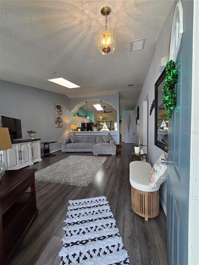 living room featuring dark wood-style floors, baseboards, visible vents, arched walkways, and a textured ceiling