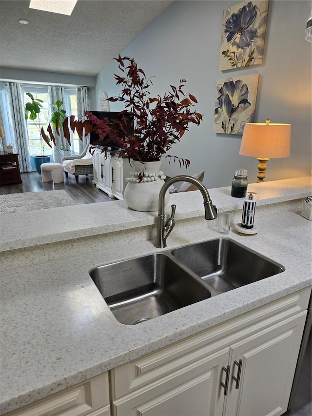 room details with light stone counters, a skylight, a sink, white cabinets, and a textured ceiling