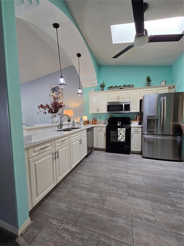 kitchen featuring lofted ceiling with skylight, a ceiling fan, a sink, appliances with stainless steel finishes, and light countertops