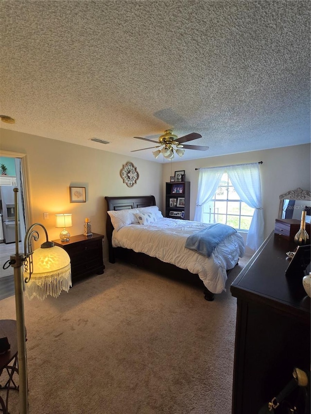 bedroom with visible vents, a ceiling fan, a textured ceiling, stainless steel fridge, and carpet