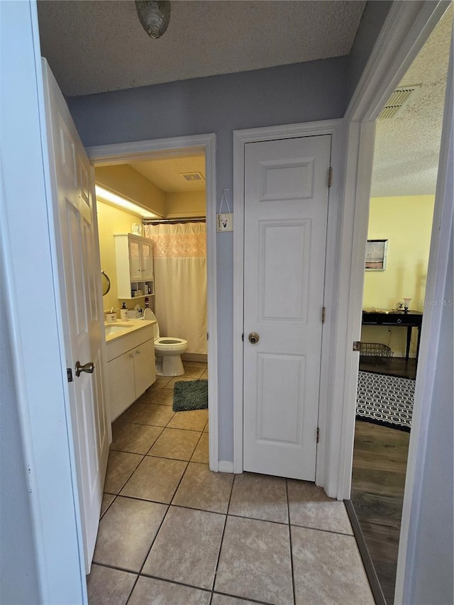 bathroom with visible vents, toilet, vanity, tile patterned floors, and a textured ceiling