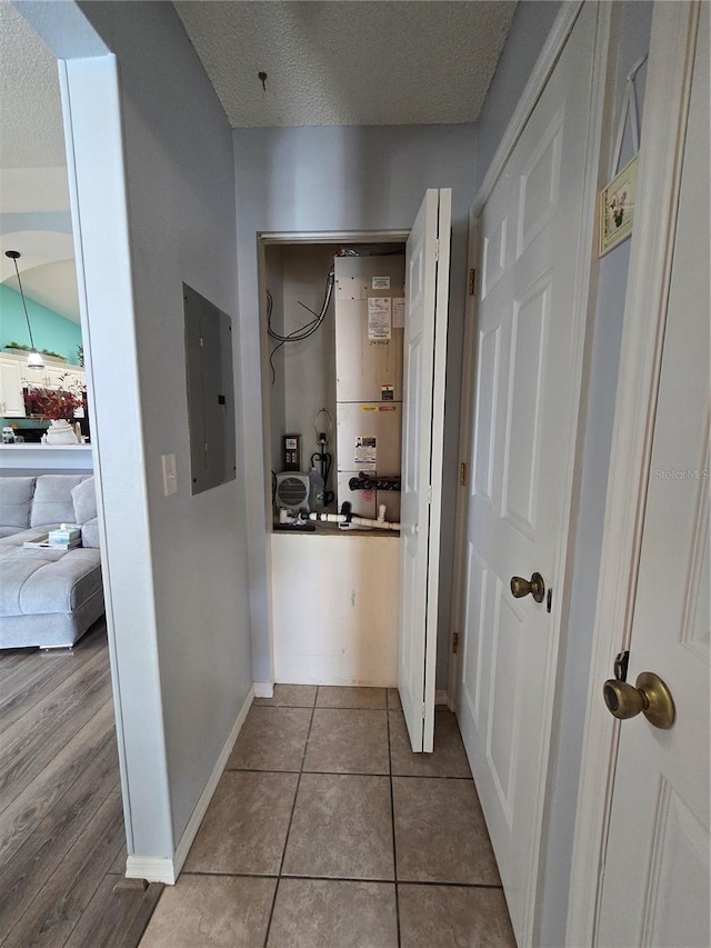 hallway with electric panel, baseboards, a textured ceiling, and tile patterned floors