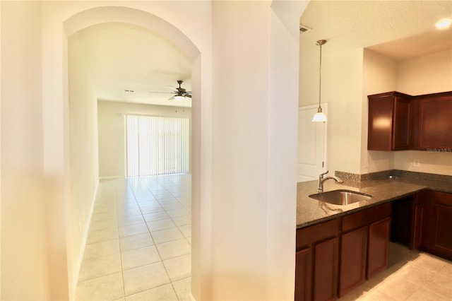 kitchen featuring a sink, dark stone counters, arched walkways, light tile patterned flooring, and ceiling fan