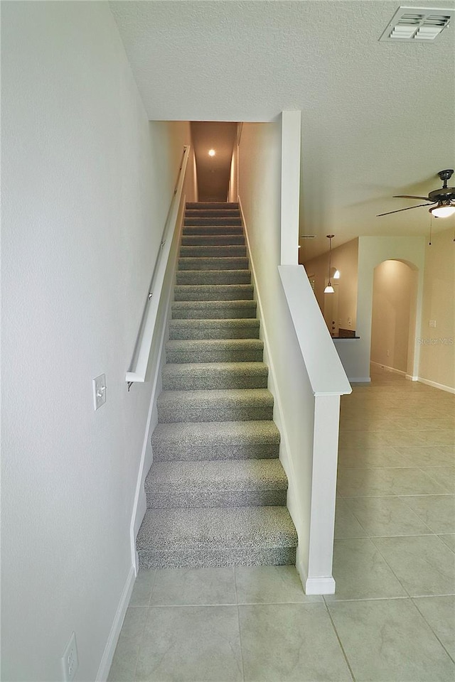 staircase featuring visible vents, baseboards, arched walkways, a textured ceiling, and a ceiling fan