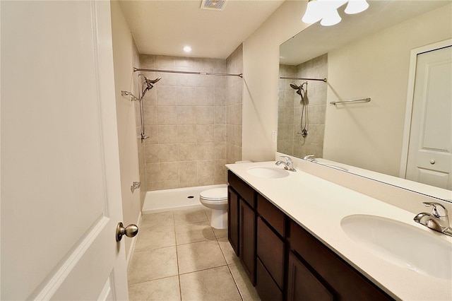 bathroom featuring a tile shower, tile patterned flooring, toilet, and a sink