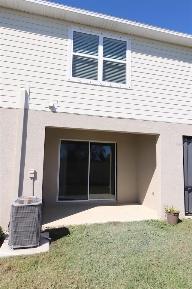 rear view of property featuring a patio area, central AC unit, a lawn, and stucco siding