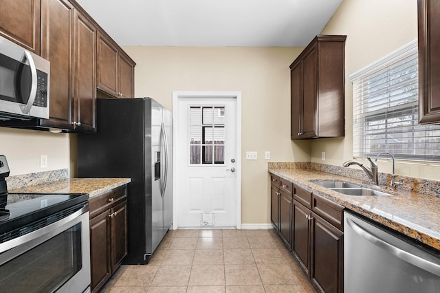 kitchen with dark brown cabinets, light stone countertops, appliances with stainless steel finishes, and a sink