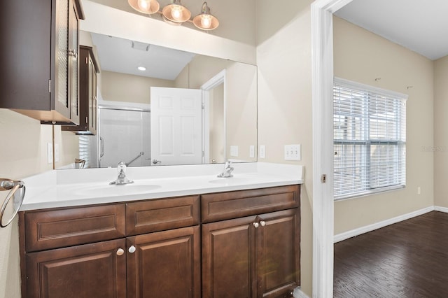 bathroom featuring baseboards, double vanity, wood finished floors, an enclosed shower, and a sink