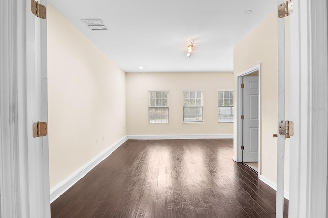 unfurnished room featuring visible vents, baseboards, and dark wood finished floors