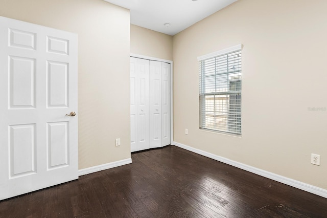 unfurnished bedroom featuring a closet, dark wood-type flooring, and baseboards