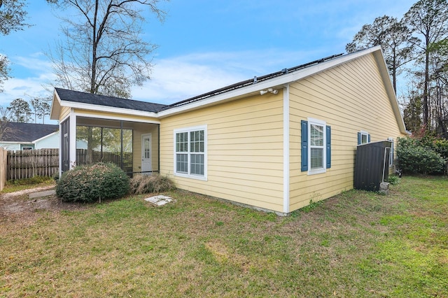 view of side of home with a lawn, a sunroom, and fence