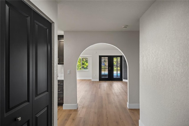 foyer entrance with light wood-type flooring, baseboards, arched walkways, and french doors