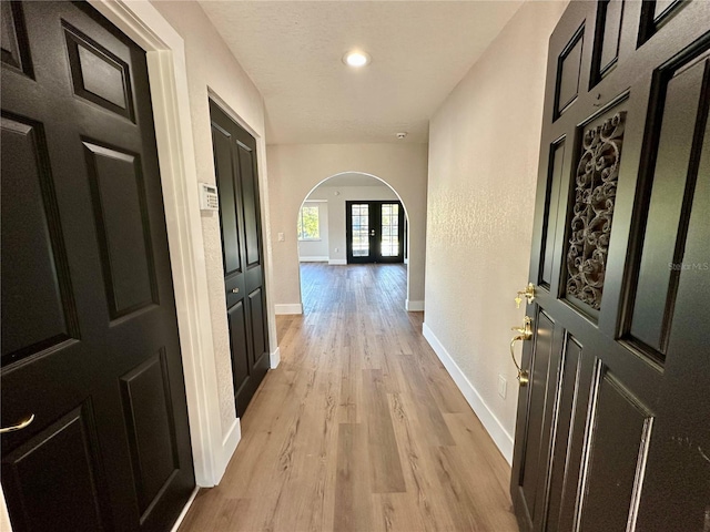 hall featuring light wood-style floors, arched walkways, a textured ceiling, and baseboards