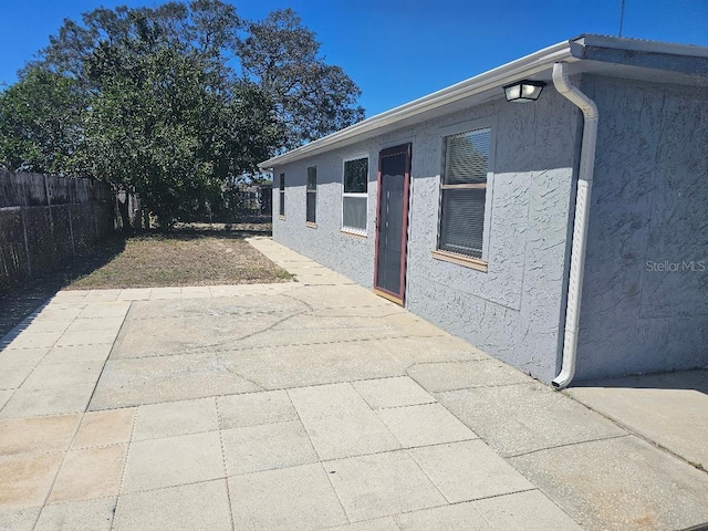 view of side of home with a patio area, fence, and stucco siding