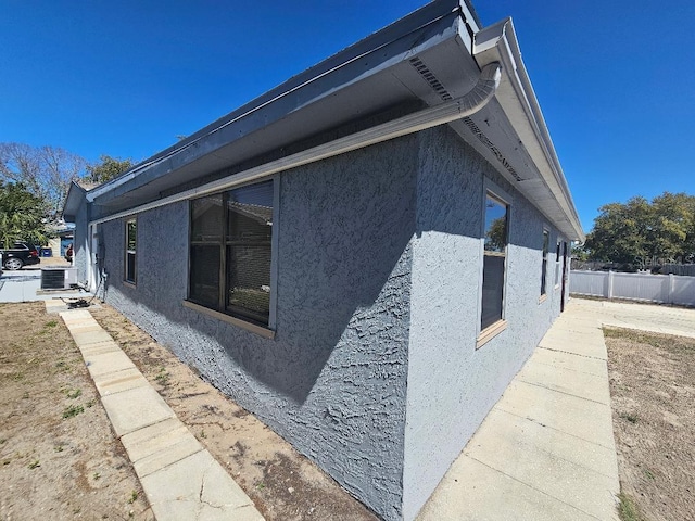 view of side of property with cooling unit, fence, and stucco siding