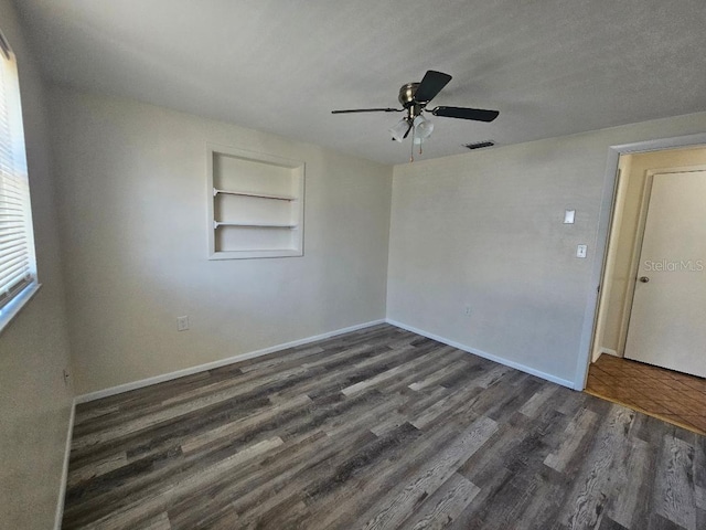 unfurnished room with visible vents, built in shelves, baseboards, ceiling fan, and wood finished floors