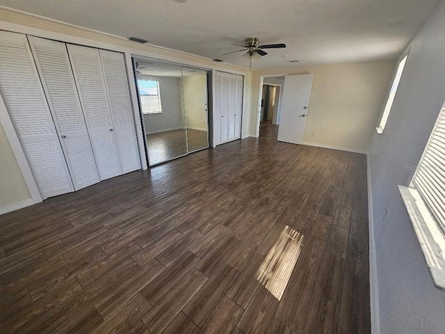 unfurnished bedroom featuring visible vents, multiple closets, baseboards, and dark wood-style floors