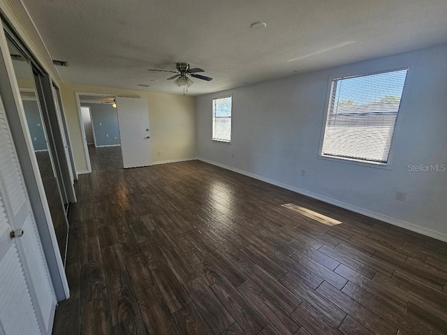 unfurnished room with visible vents, baseboards, dark wood-style floors, and a ceiling fan