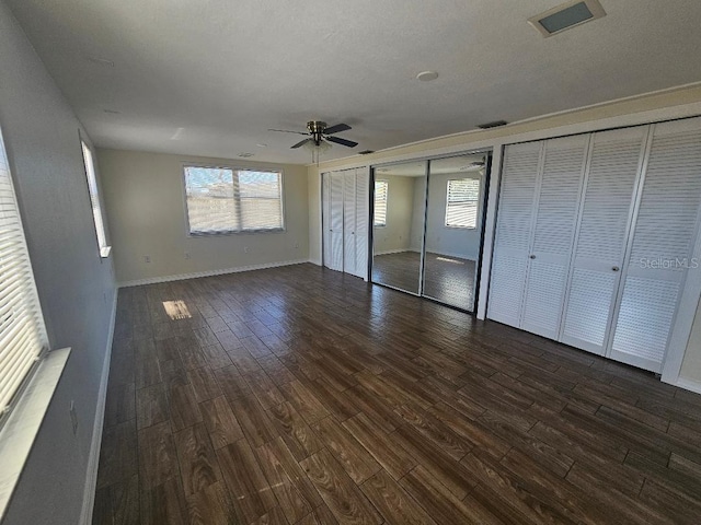 unfurnished bedroom with dark wood-style floors, visible vents, two closets, and baseboards