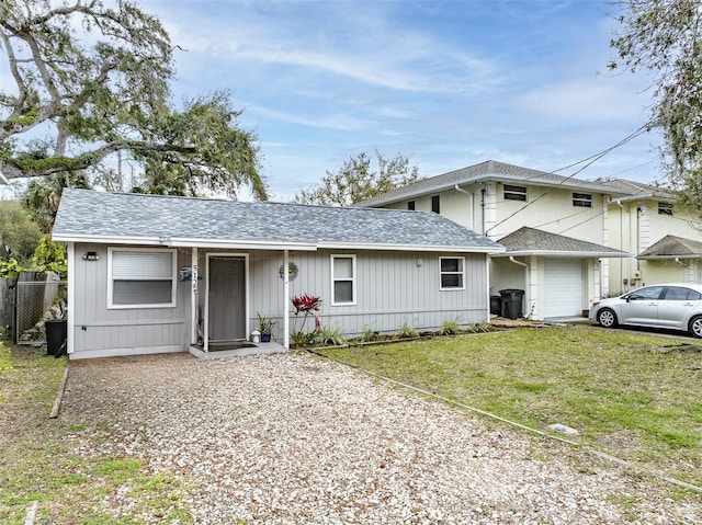 view of front of home featuring a front lawn, fence, gravel driveway, roof with shingles, and an attached garage