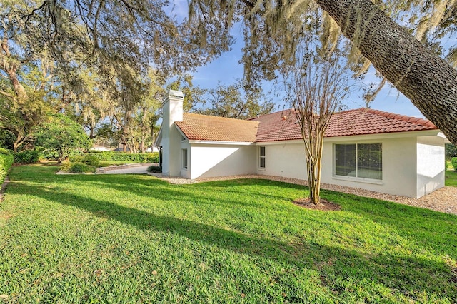 back of house with a lawn, a tiled roof, a chimney, and stucco siding