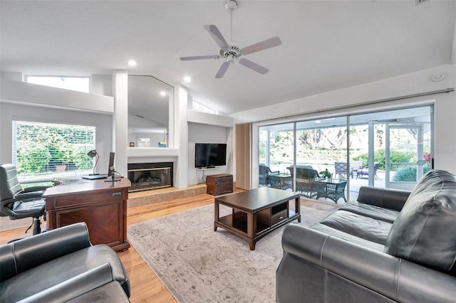 living area with a glass covered fireplace, lofted ceiling, light wood-style floors, and a wealth of natural light