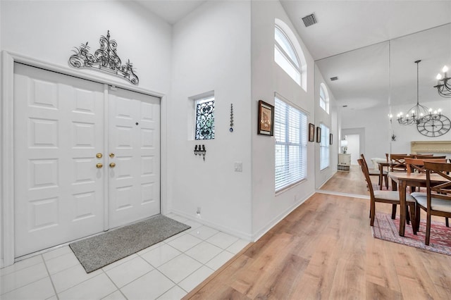 foyer entrance featuring visible vents, a notable chandelier, a high ceiling, light wood finished floors, and baseboards