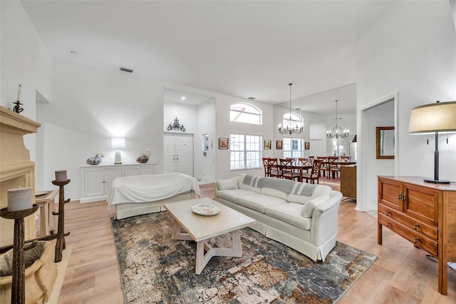 living area featuring a high ceiling, a notable chandelier, light wood-style floors, and visible vents