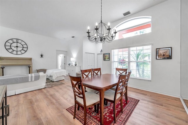 dining space with visible vents, a notable chandelier, a high ceiling, light wood-style floors, and baseboards