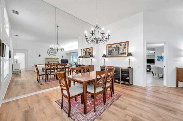 dining area featuring visible vents, a notable chandelier, light wood-style flooring, and a towering ceiling