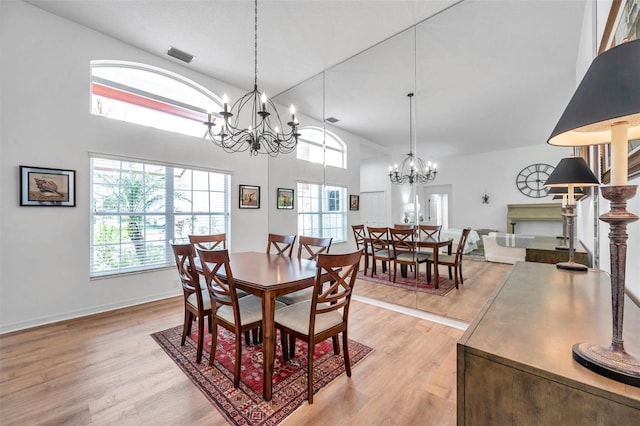 dining area featuring light wood-style flooring, visible vents, a chandelier, and a towering ceiling